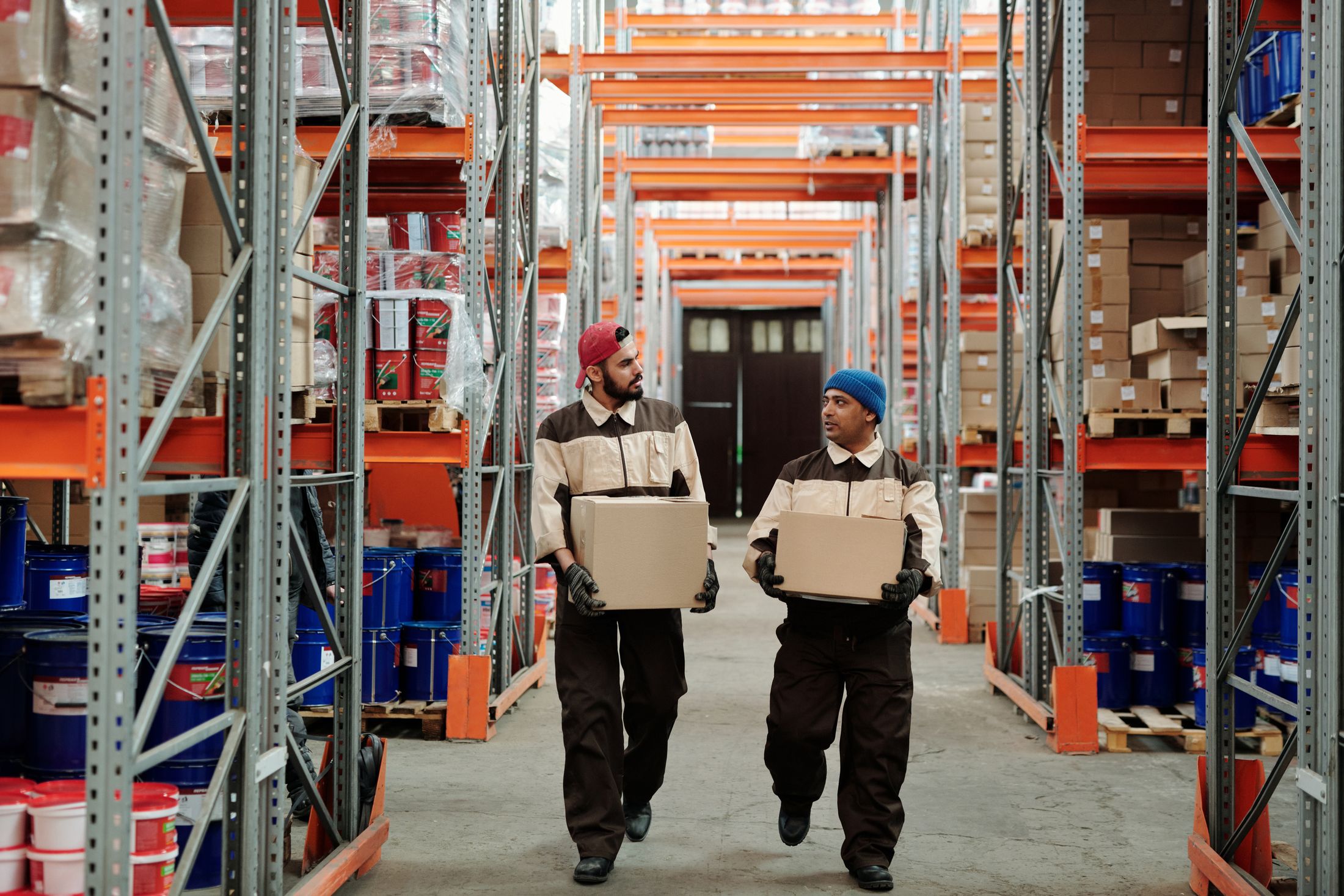 Two warehouse workers carrying parcels through a storage aisle